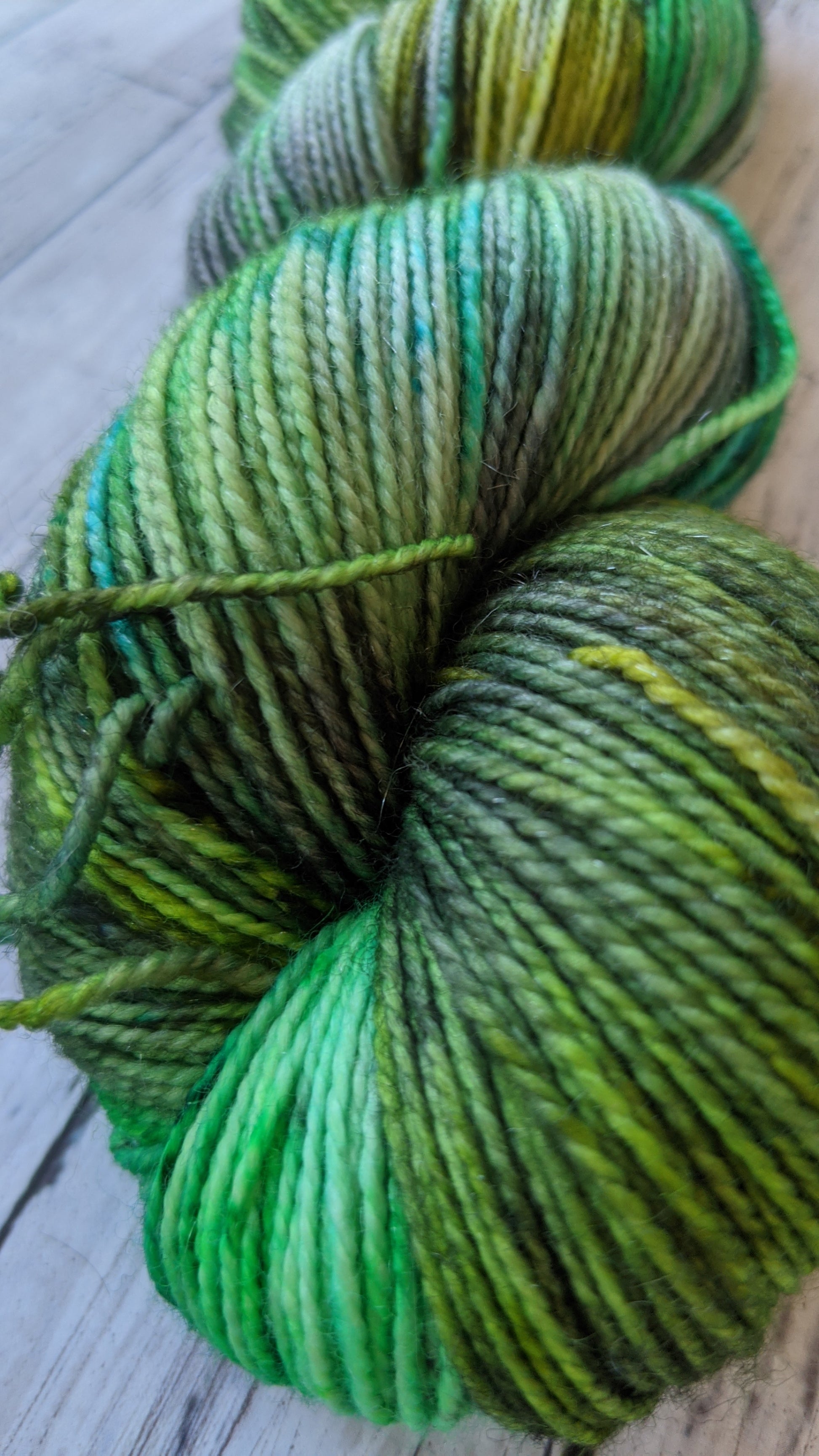 close up of hand dyed various shades of green yarn with black speckles